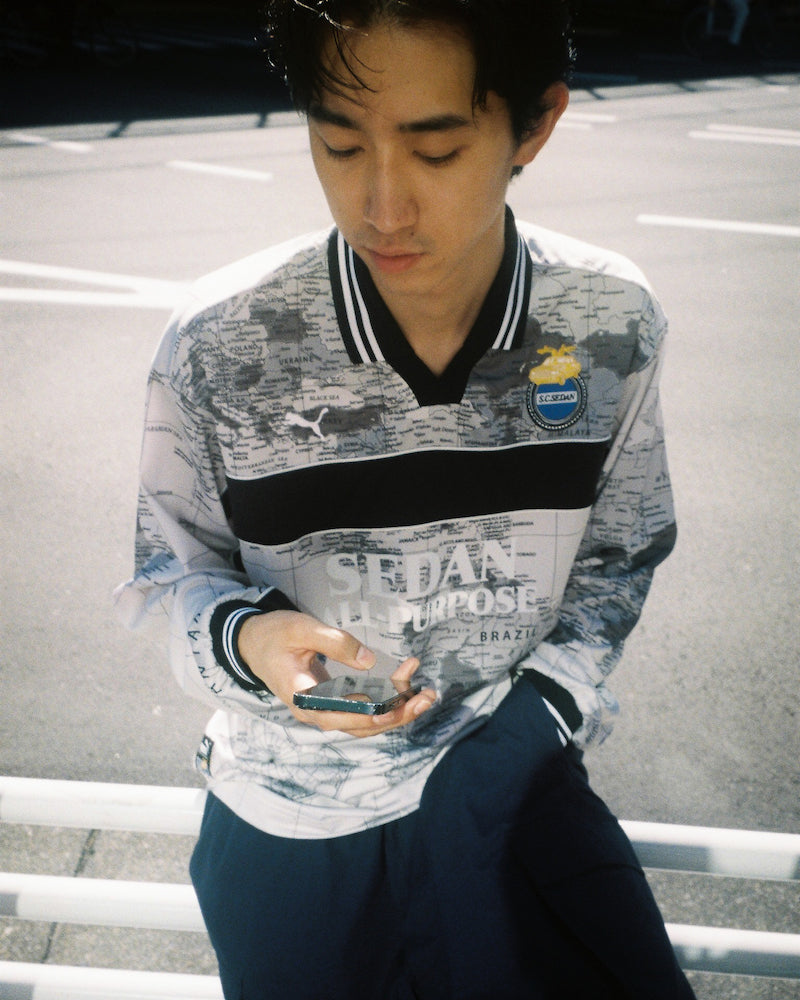Model on a street railing in the PUMA x SEDAN ALL-PURPOSE World Map Game Shirt with the S.C.SEDAN crest, from the official lookbook. Photo via Houyhnhnm