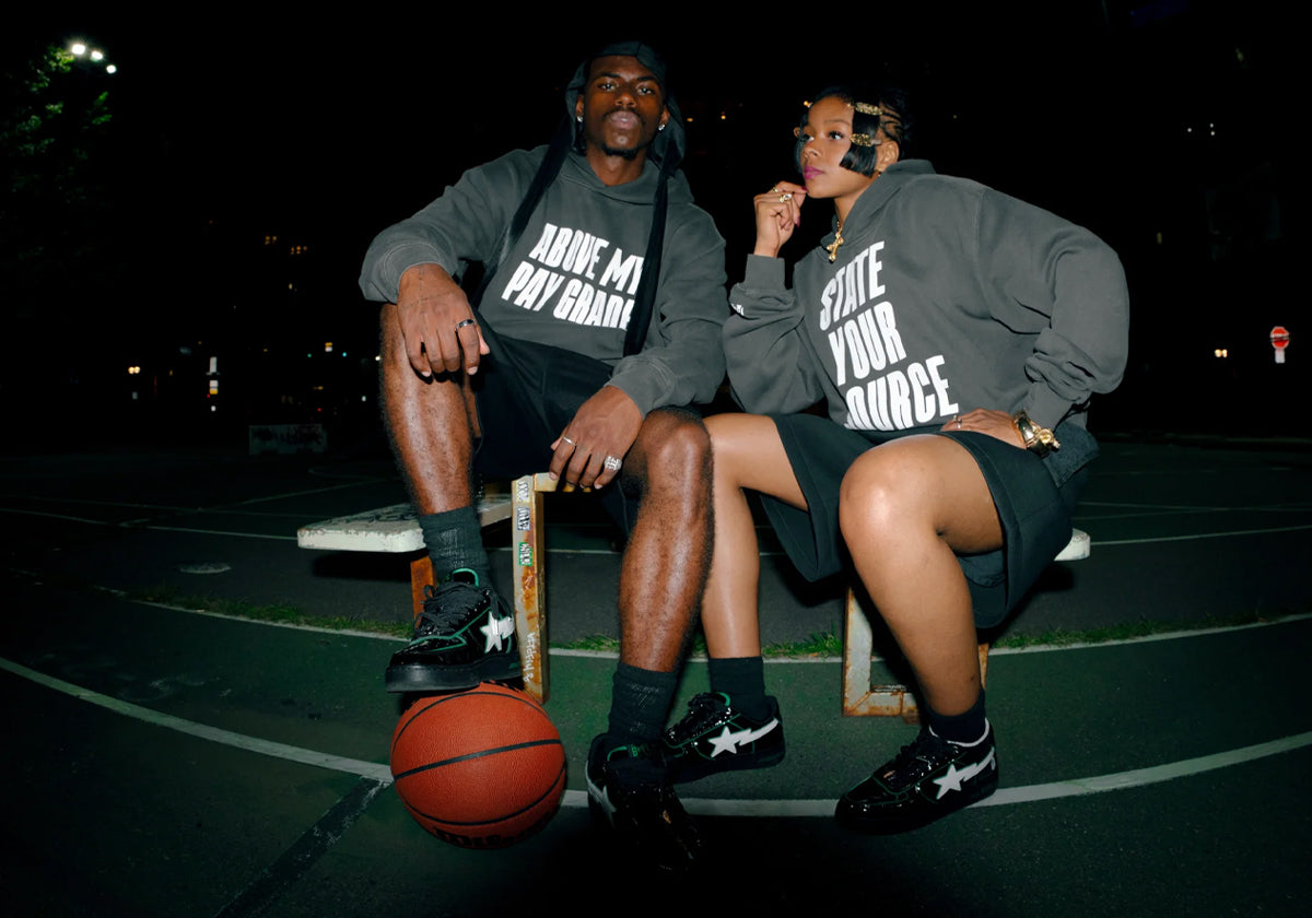 7UICE x BAPE STA in black patent leather with white star and green piping, worn on a basketball court at night — campaign image via Sneaker News