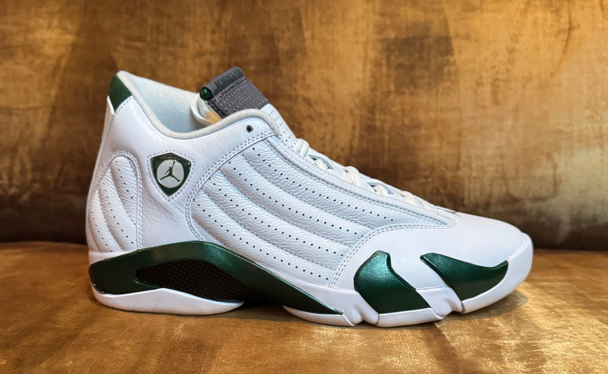 Air Jordan 14 Retro Forest Green 487471-300 in white leather with deep green accents, shot on a gold velvet couch. Photo via Complex