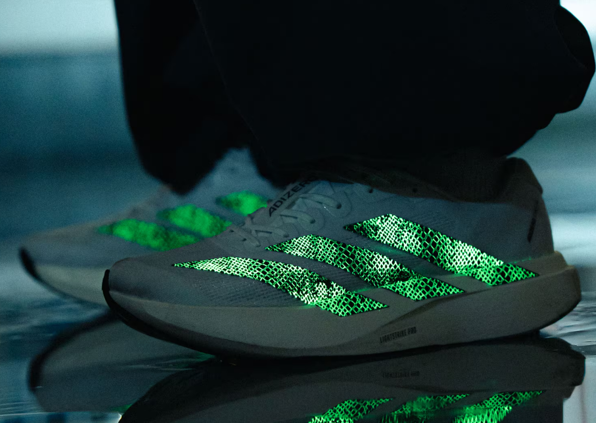atmos x adidas Adizero Evo SL G-SNK White on foot with glow-in-the-dark snakeskin stripes lit green. Official image via Sole Retriever