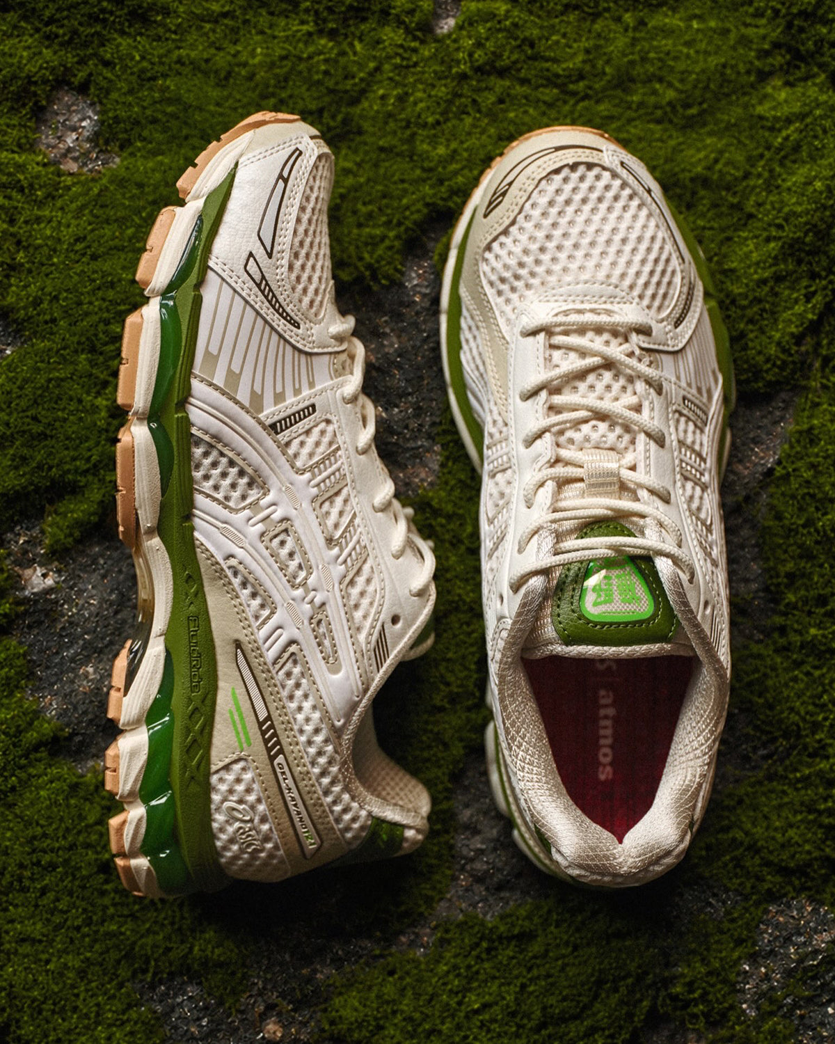 atmos x ASICS GEL-Kayano 12.1 Archipelago pair in cream and grey with a forest-green midsole, shown from above on a bed of green moss. Photo via Sneaker News