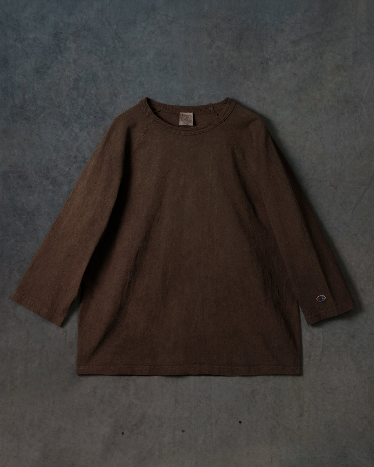 Champion Made in USA T1011 AMAMI DOROZOME long sleeve — mud-dyed dark brown flat on textured press backdrop — official Champion Japan