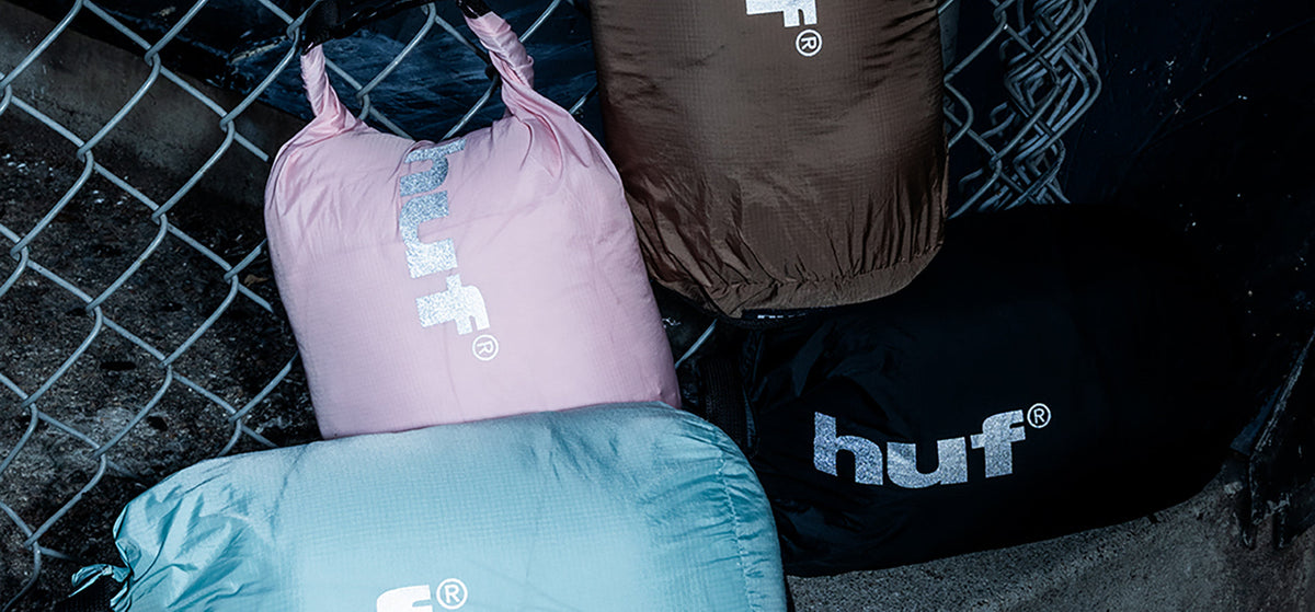 HUF × TAION FW26 packable down stuff sacks on concrete against a chain-link fence — HUF Japan environmental still