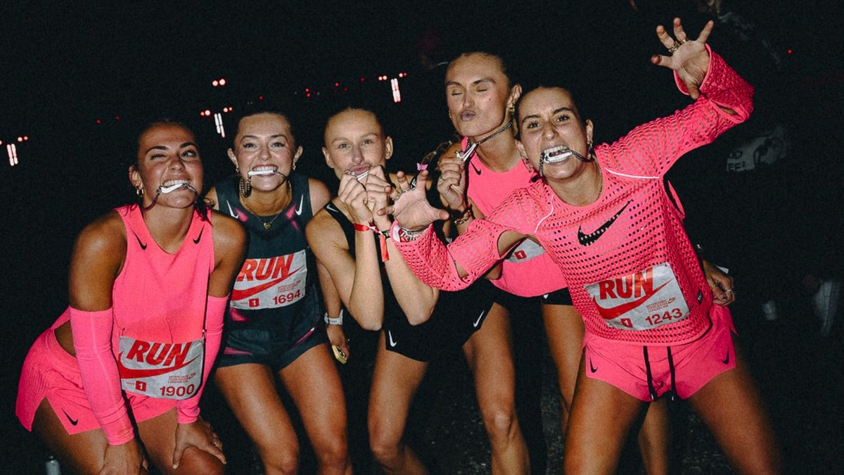 Runners in pink Nike kits and RUN bibs biting their medals after the Nike After Dark Tour London 10K. Photo by @marymccarths via House of Heat
