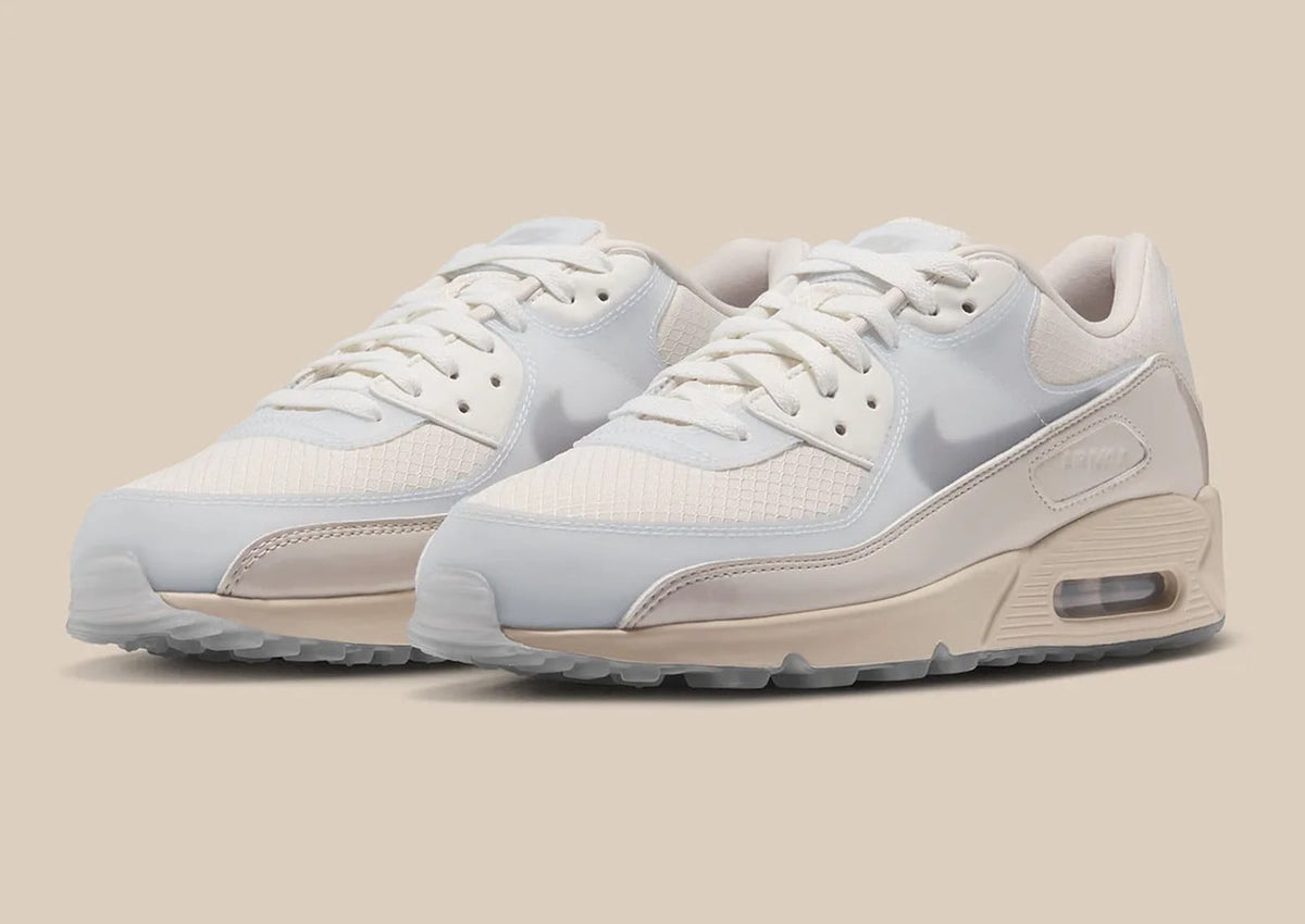 Pair of Nike Air Max 90 "Light Orewood Brown" IX8056-104 sneakers in sail and light brown with grey Swooshes, on a tan backdrop. Nike image via JustFreshKicks