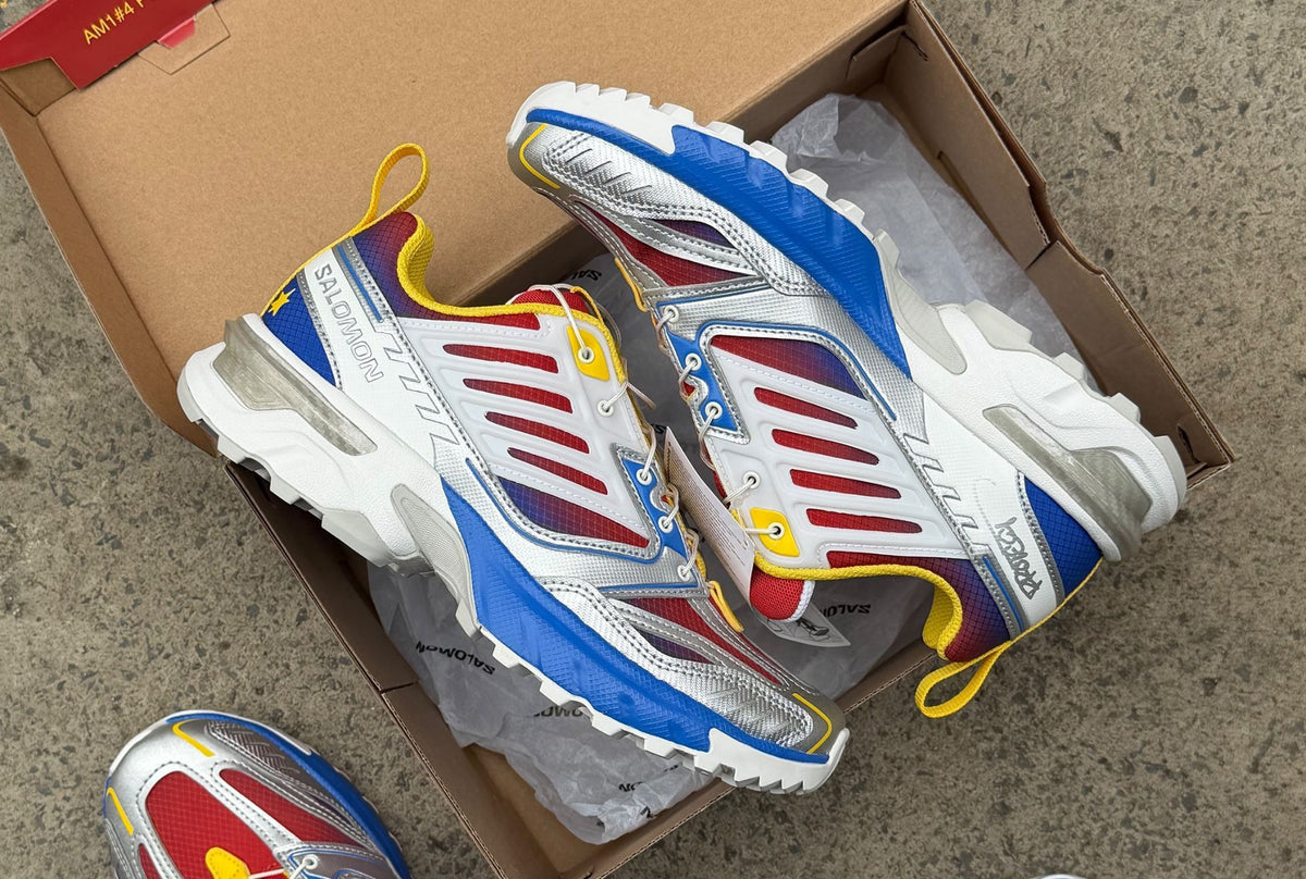 PROTECT x Salomon ACS NEXXT 'Slushie' in a box, with a red and blue gradient upper, silver overlays, yellow pull tabs and blue midsole. Photo via Sneaker Freaker