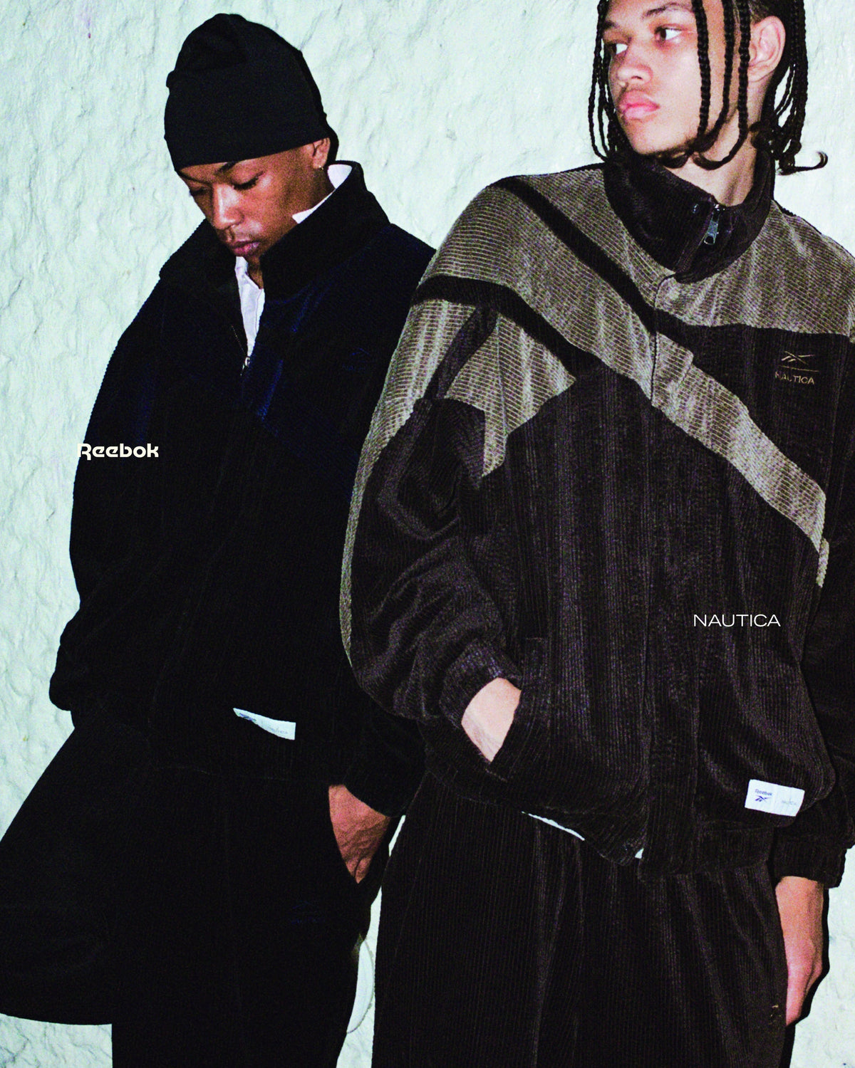 Two models in Reebok × NAUTICA corduroy track jackets with the Reebok vector logo against a white plaster wall — official campaign image