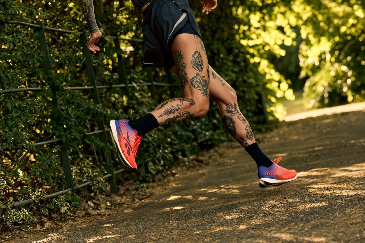 Runner mid-stride on a leafy park path wearing the Reebok SpeedShifter in Red/White/Blue. Photo via Reebok