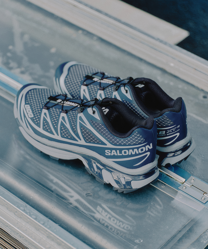 A pair of Salomon XT-6 Steel Streets sneakers in Spellbound, Tradewinds and Dark Navy resting on a sheet of steel and glass