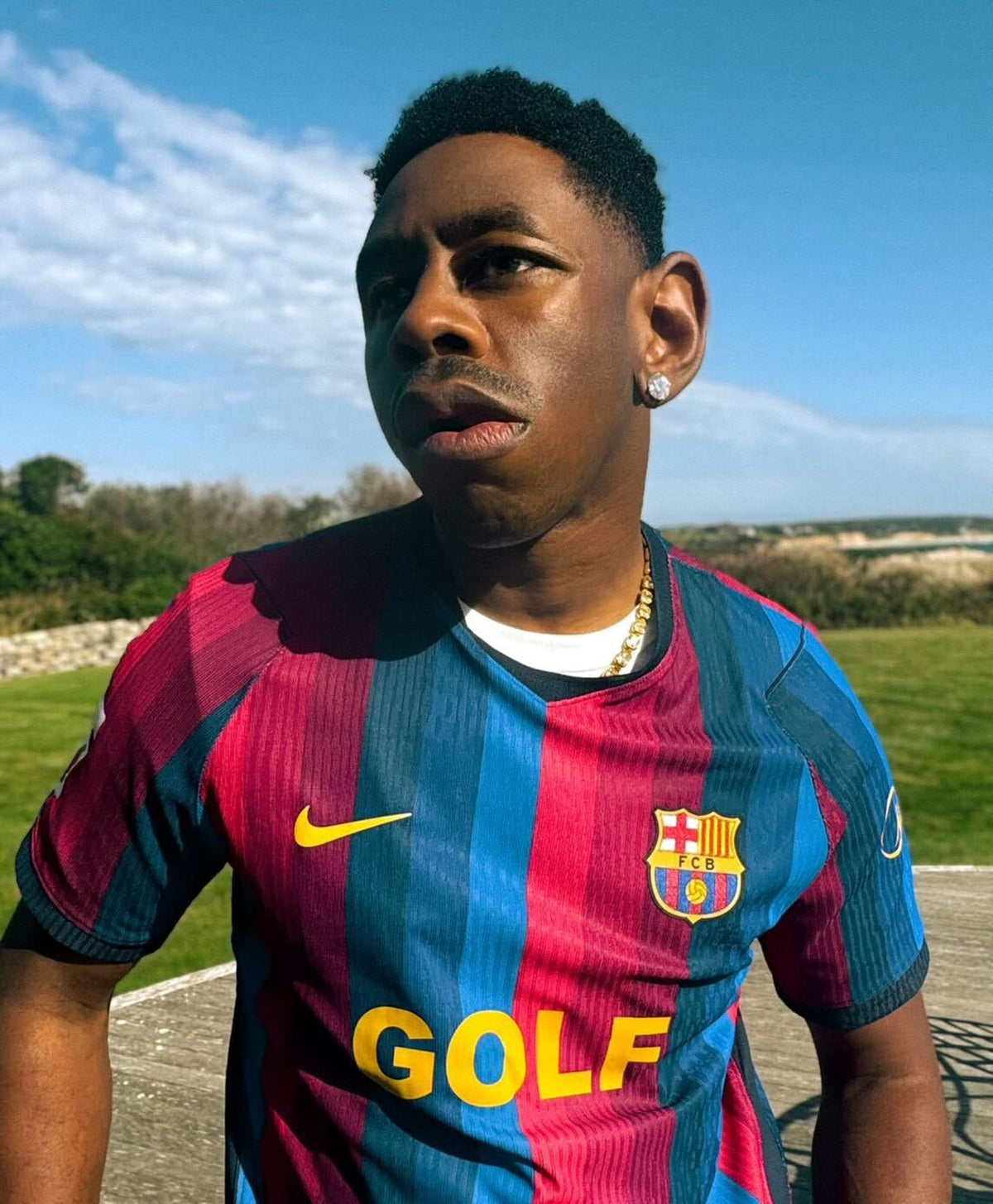 Tyler, the Creator wearing the FC Barcelona home jersey with a gold GOLF logo outdoors, official FC Barcelona photo